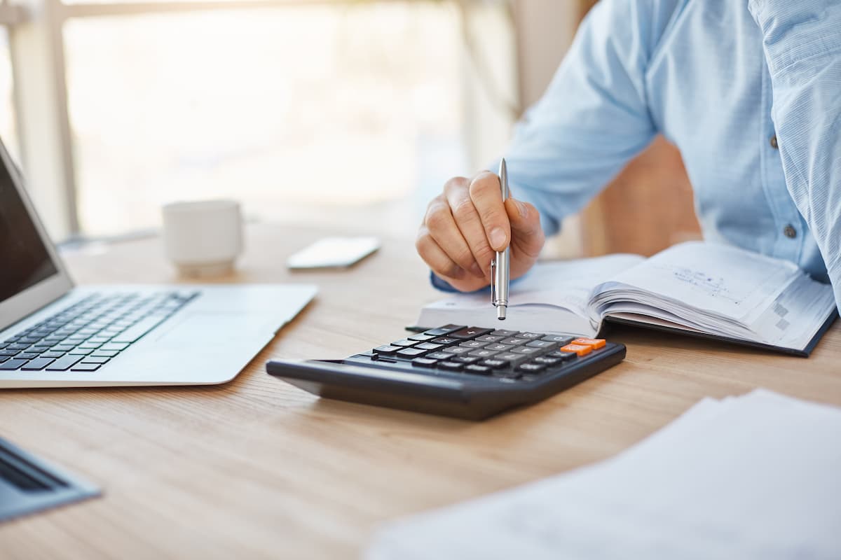 Extinción de condominio. Una persona sobre una mesa usando una calculadora, con un bolígrafo, ordenador y papeles alrededor