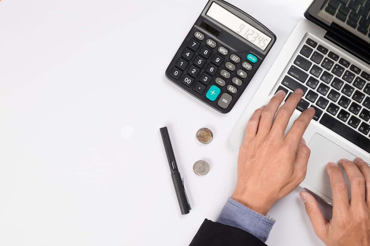 Calculadora, monedas y bolígrafo y las manos de una persona trabajando en un ordenador